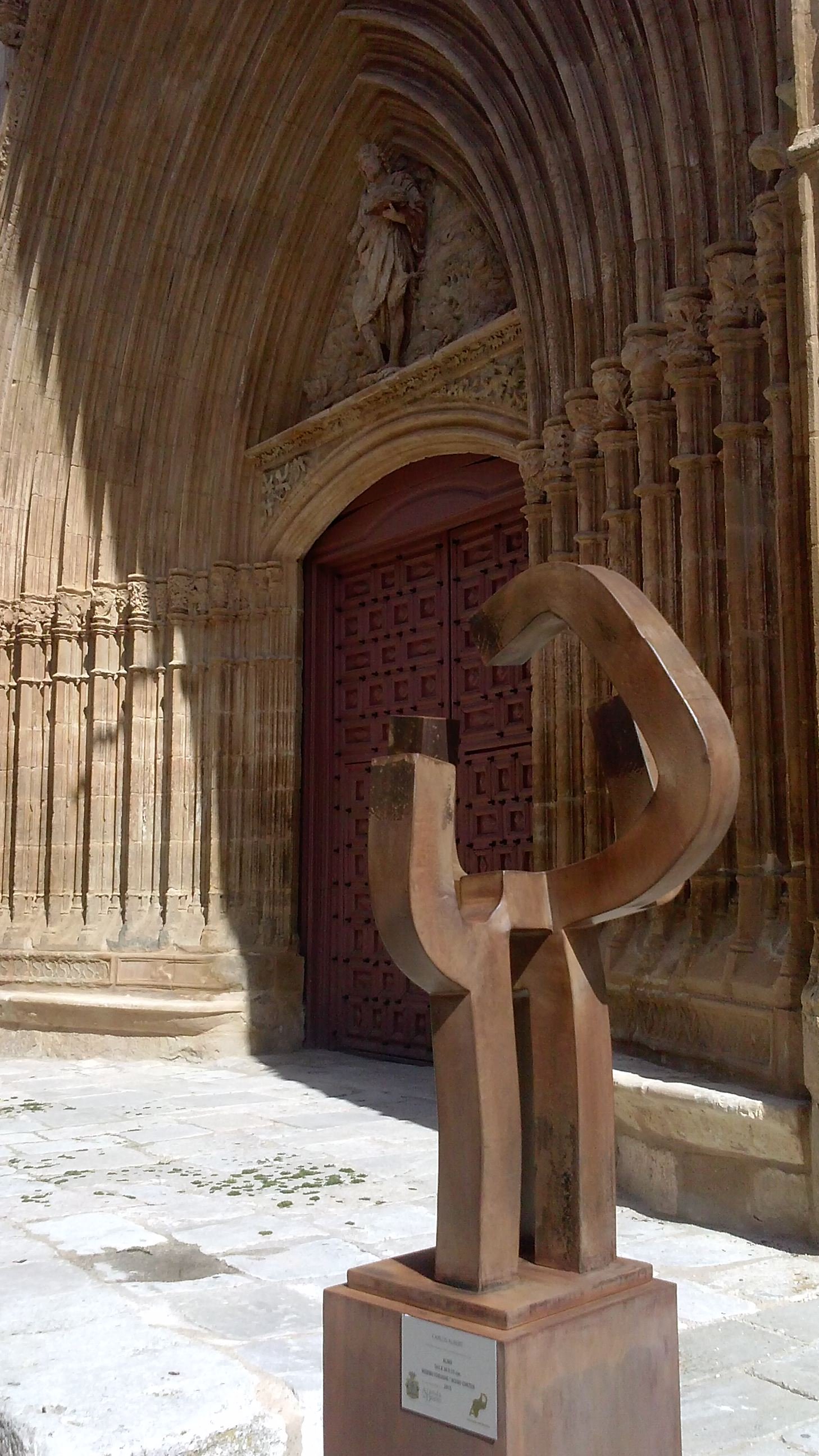 Almo, 163 X 38 X 35 cm, hierro forjado / Acero corten, 2015, pieza única. Como una sencilla aureola, la escultura se desarrolla a partir de un arco en la parte superior de la obra, homenaje a San Juan Bautista. Los tres apoyos verticales y el pedestal sobre el que se sitúa, aportan espiritualidad a la pieza.