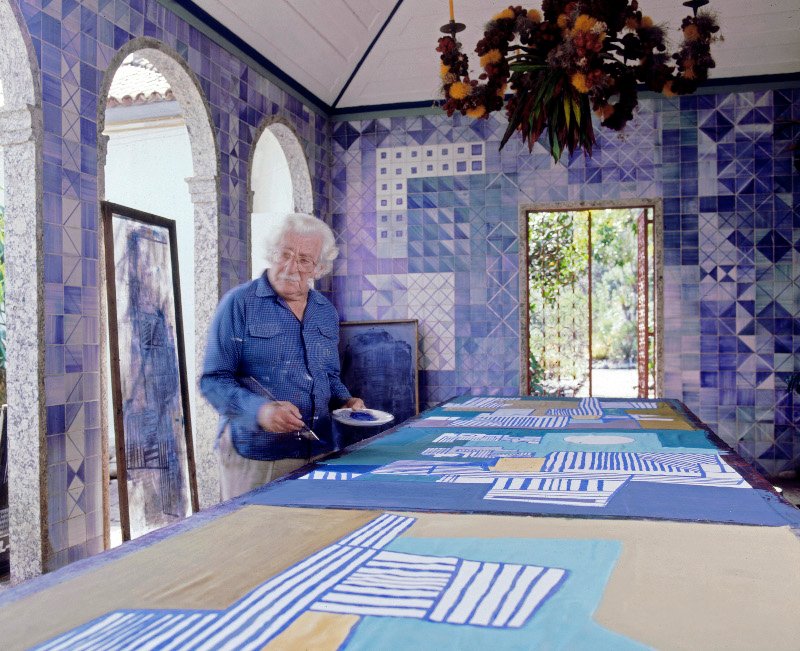Roberto Burle Marx pintando un mantel en su casa en los años 80. El azulejo de los muros y el candelabro de frutas y flores sobre estructura de y metal son diseños suyos. Fotografía © Tyba