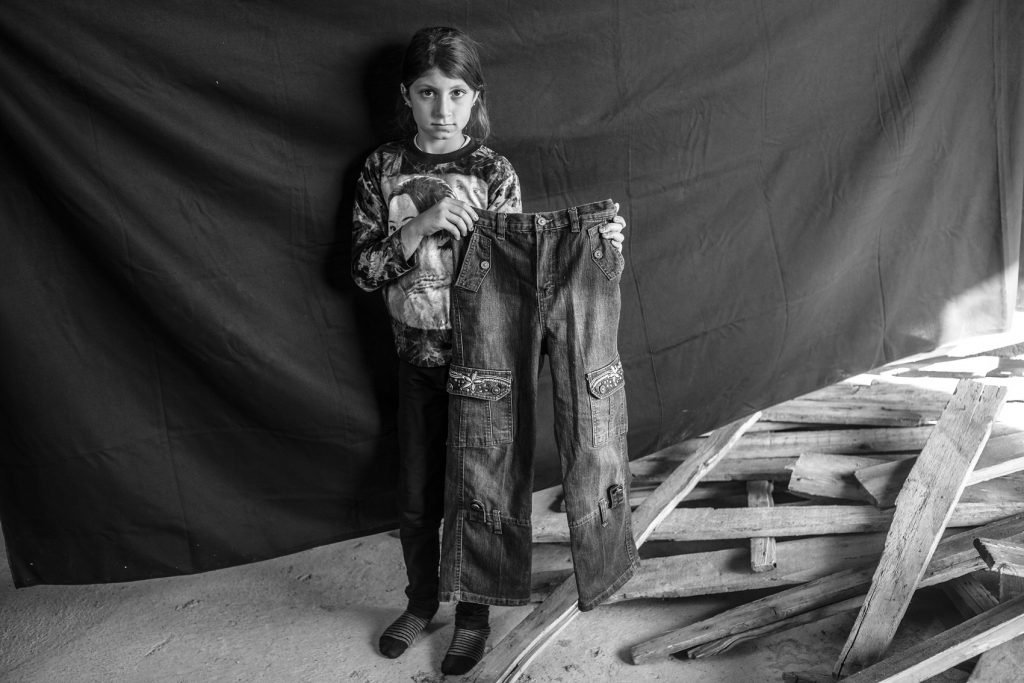 Leila, 9 años, en Erbil, Kurdistán, Iraq (17 de noviembre de 2012). Con sus cuatro hermanas, su madre, su padre y su abuela, llegó a Erbil huyendo de Deir ez-Zor, Siria. Dice, sobre lo más espeluznante antes de su huida: «Era el sonido de los tanques, incluso más aterrador que el de los aviones, porque sentía como que los tanques venían a por mí». Lo más importante que Leila pudo llevarse son los pantalones que sujeta en esta fotografía. «Cuando vi estos pantalones, supe al instante que eran perfectos, porque tienen una flor y me encantan las flores». Solo los ha usado en tres ocasiones, todas ellas en Siria.