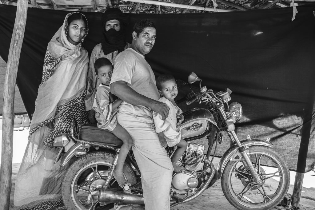 Abdou Ag Moussa, 34 años, en el campo de refugiados de Mentao, Burkina Faso. Abdou está sentado junto a su familia sobre la moto que asegura que le salvó la vida. La familia de Abdou huyó de su casa en Malí después de que su madre y otras cuatro mujeres fueran secuestradas, llevadas al desierto y asesinadas. Cuando Abdou se enteró de lo que había sucedido, esperó a que oscureciera y escapó con su esposa y sus dos hijos al desierto. Volvió a los pocos días para enterrar a su madre, y luego metió a su esposa e hijos en un coche mientras él y su padre les seguían en la moto.